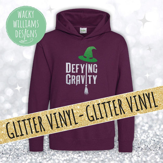 A plum hoodie with defying gravity written on in sparkly silver with a broom and green sparkly witches hat