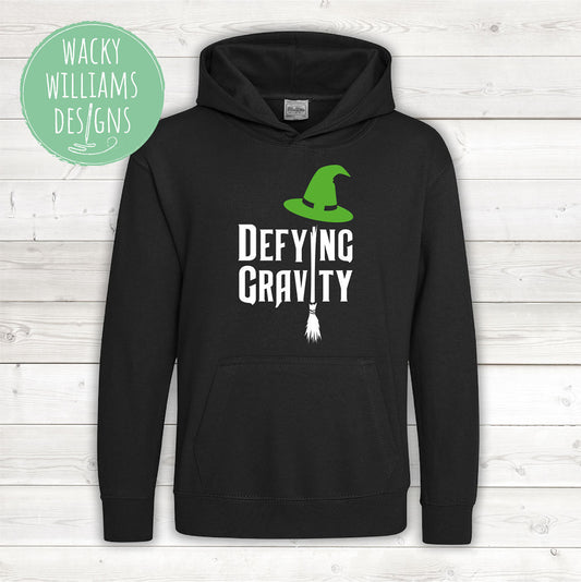 A black hoodie with defying gravity written on in white with a broom and green witches hat